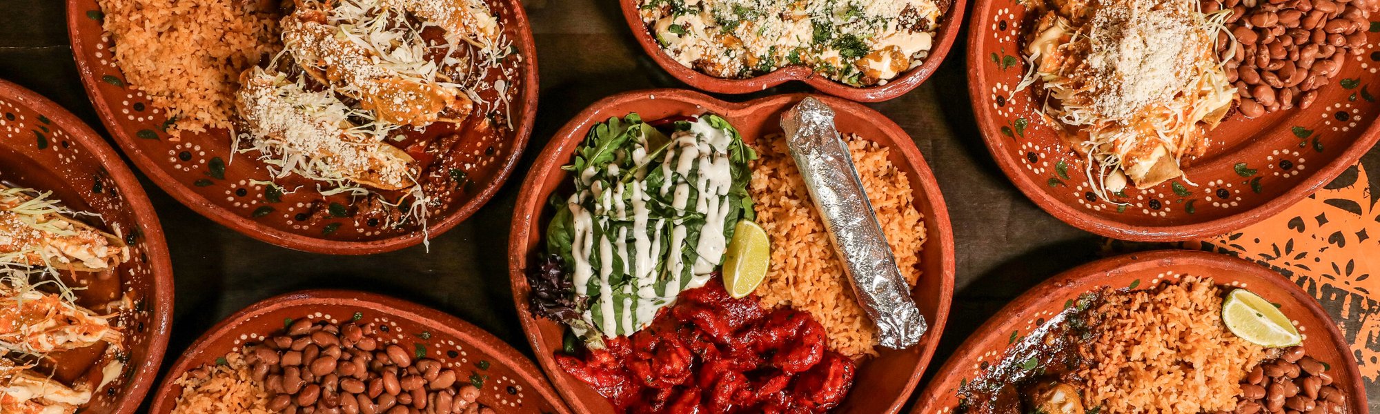 A wide overhead spread of tacos, birria and sides across the table