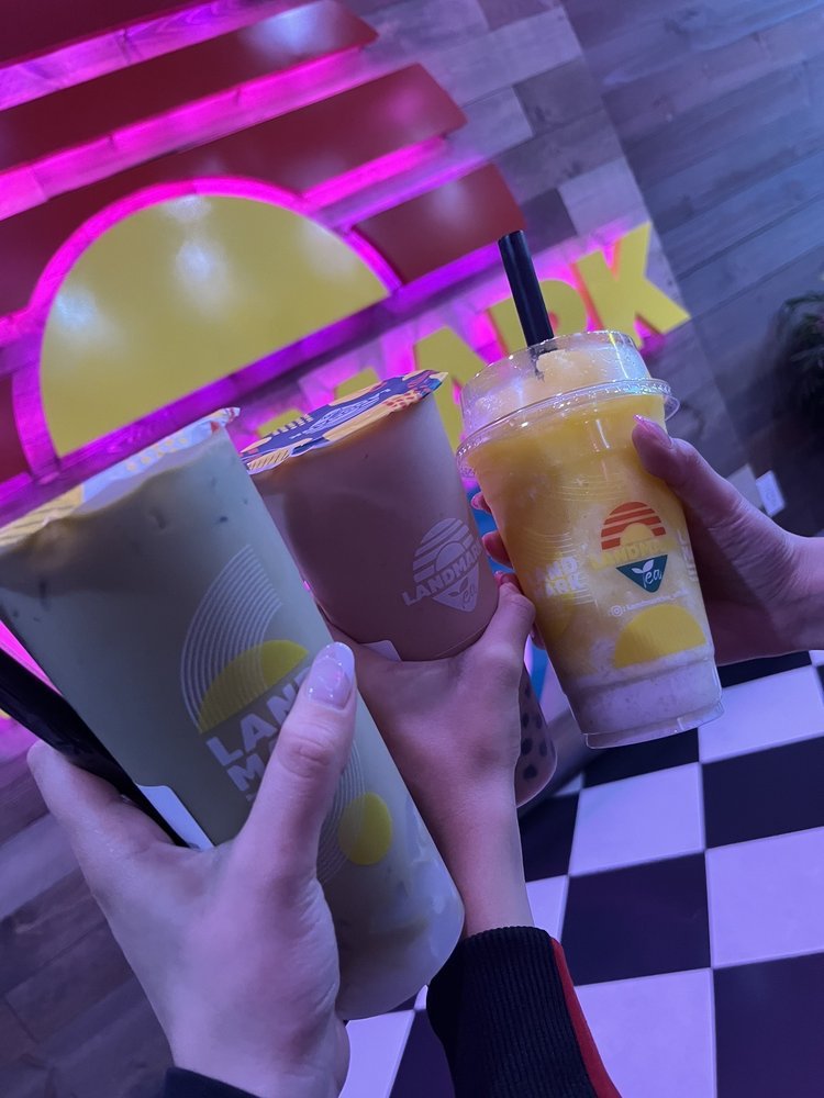 Friends cheersing their drinks under the neon Landmark logo
