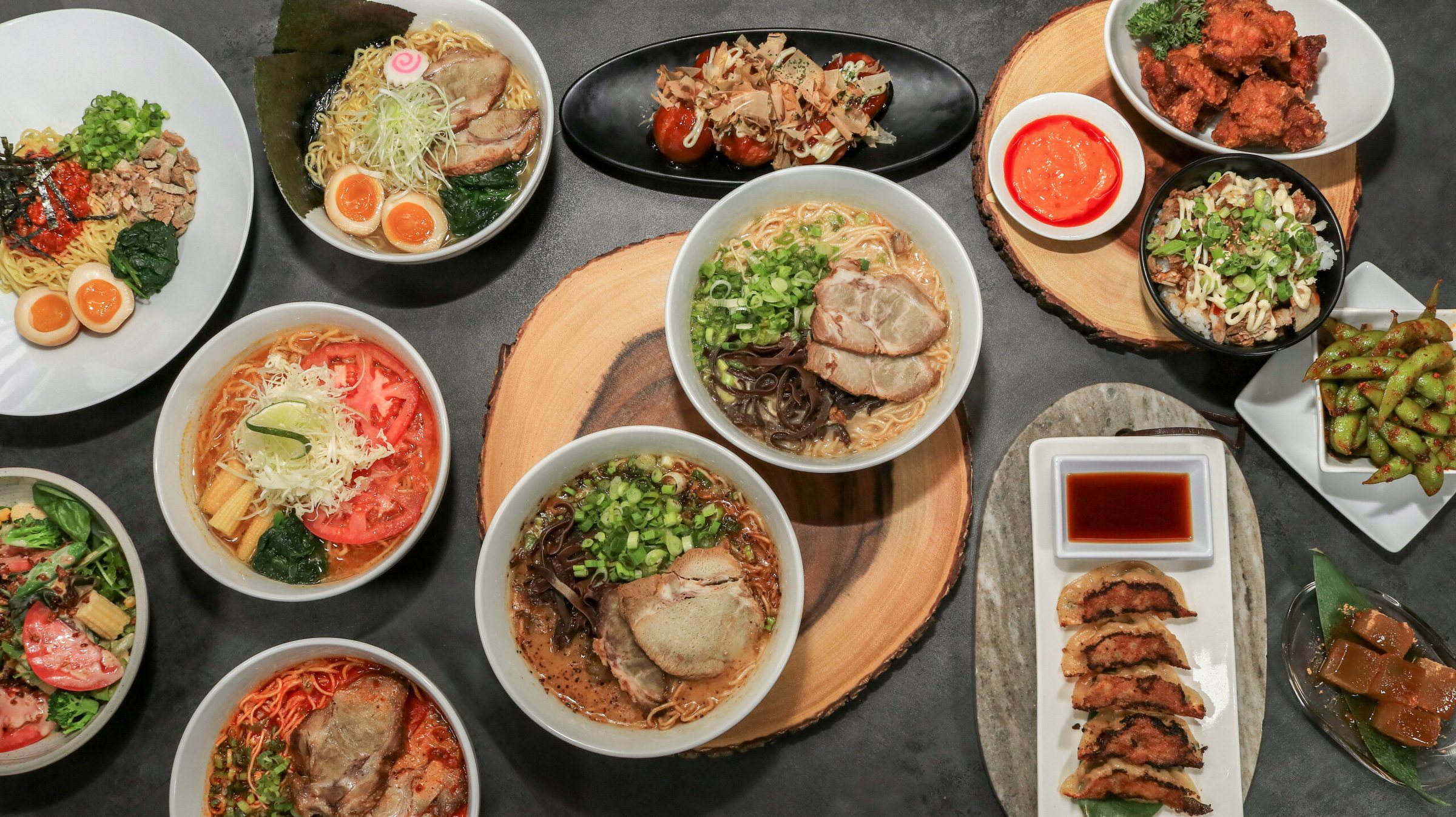A spread of tonkotsu ramen bowls, gyoza and sides on a wooden table