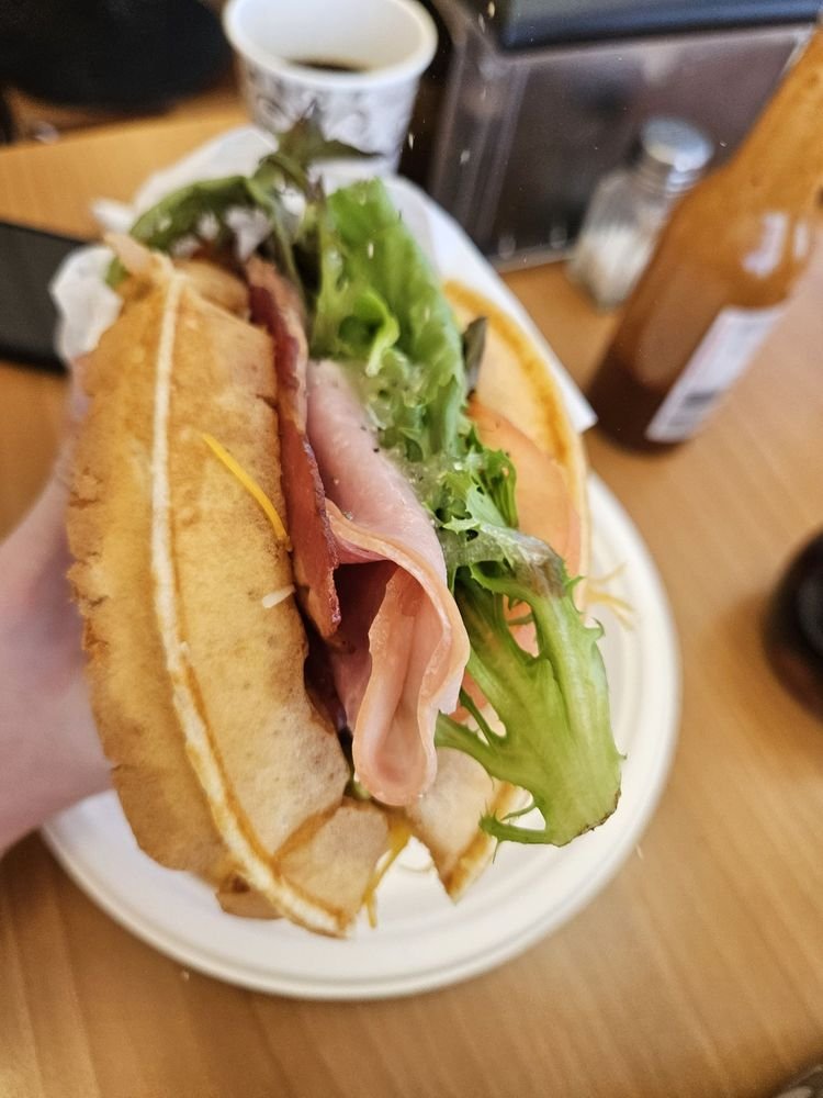 Ham and bacon waffle sandwich held in hand, filled with greens and tomato